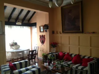A living room with a striped sofa, red pillows, a coffee table, and a dining area with a round table and chairs. A painting hangs on the wall.