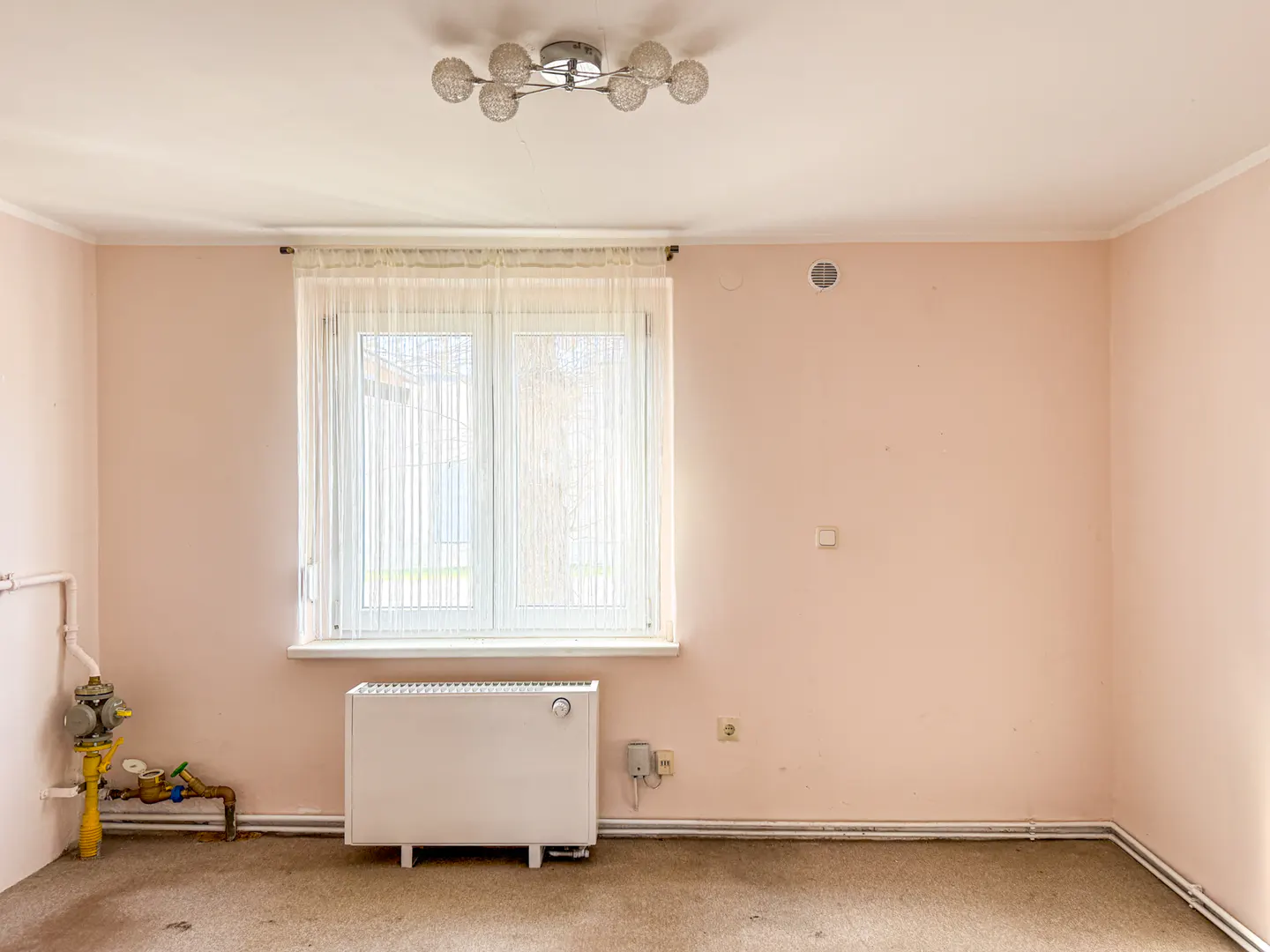 Empty room with pink walls, a window with sheer curtains, and a white radiator. A light fixture is on the ceiling.