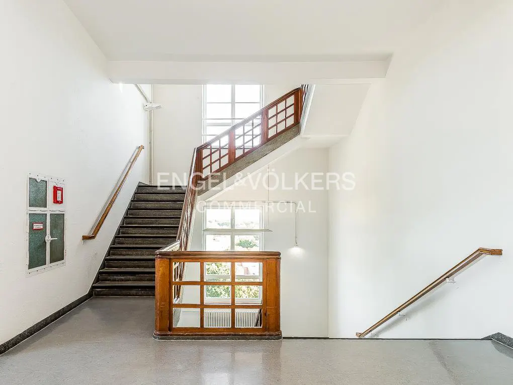 Bright, white stairwell with dark stairs and wood railings. A fire hose cabinet is on the left wall. Engel & Völkers logo is visible.