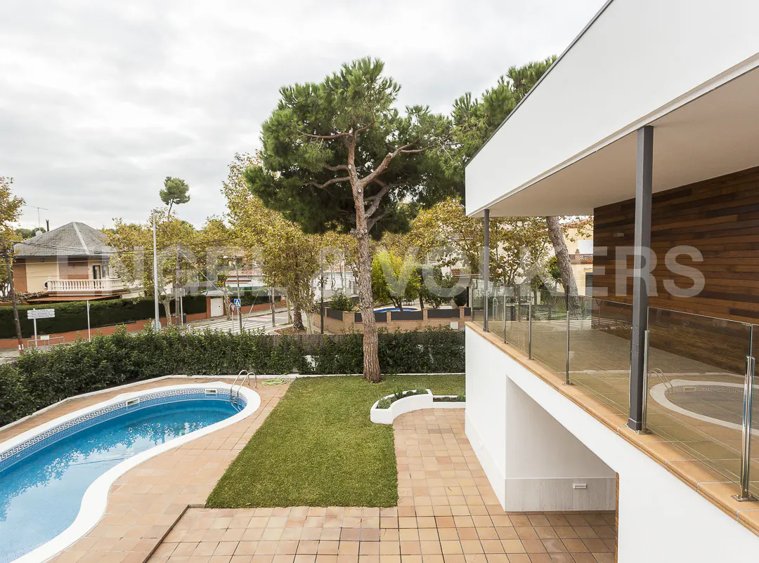 Aerial view of a modern house with a blue pool, green lawn, and brick patio on a cloudy day.