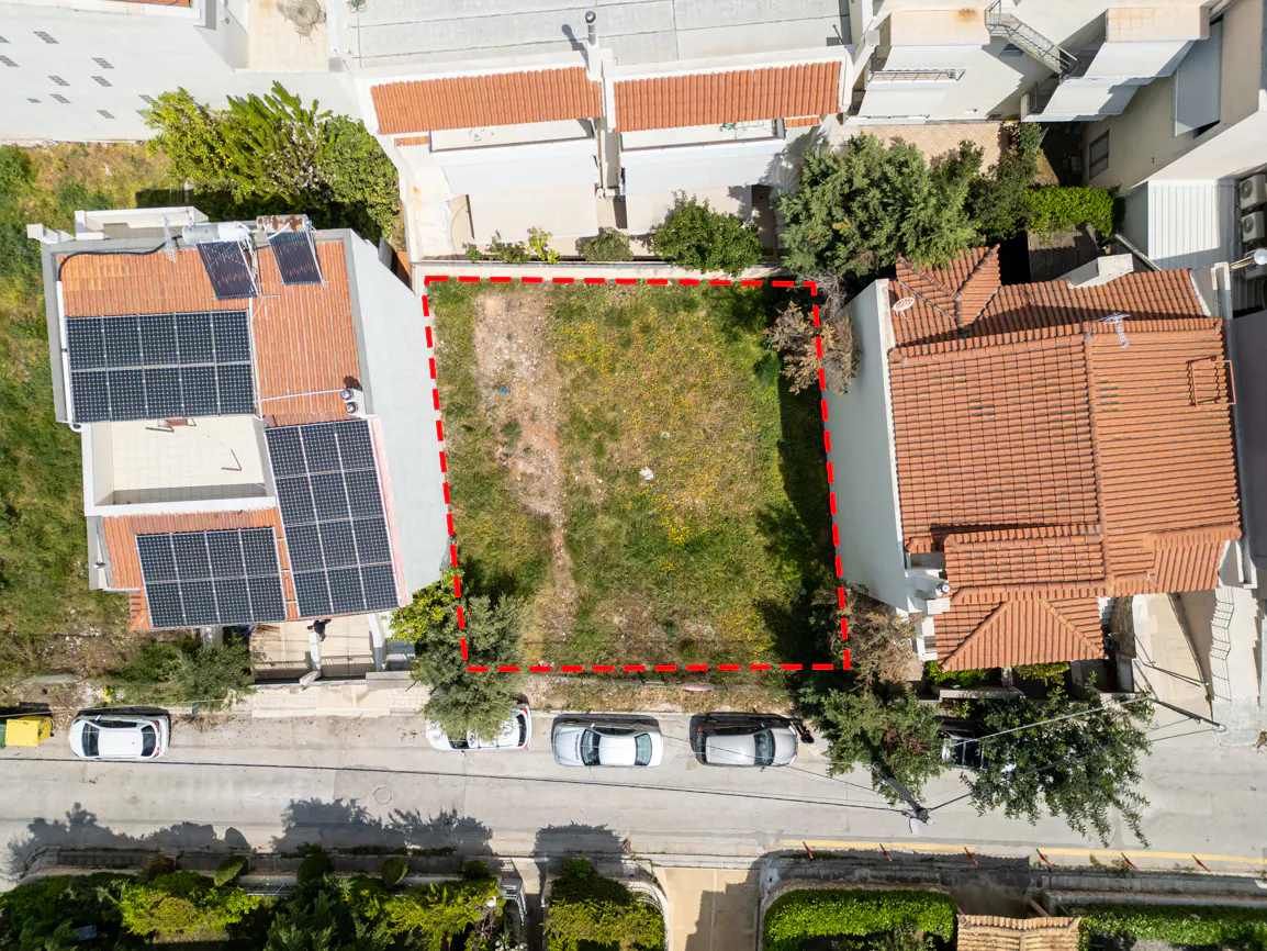 Aerial view of a vacant lot outlined in red, surrounded by houses and a street with parked cars.