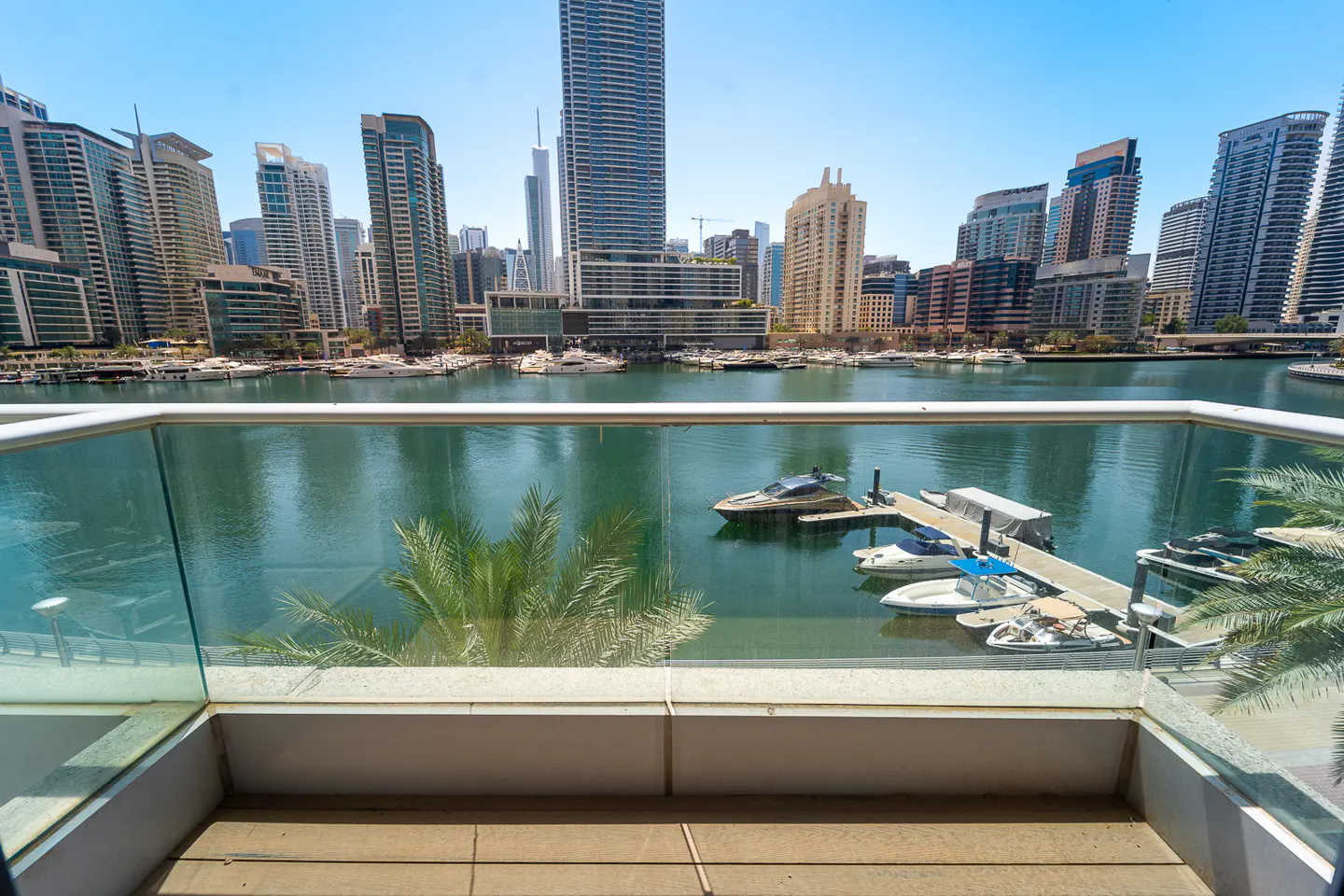 View from a balcony overlooking a marina with yachts and skyscrapers in the background on a sunny day.
