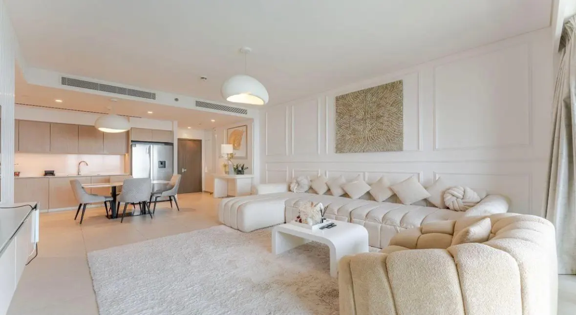 Bright, modern living room with white walls, a plush sectional sofa, and a dining area with a table and chairs.