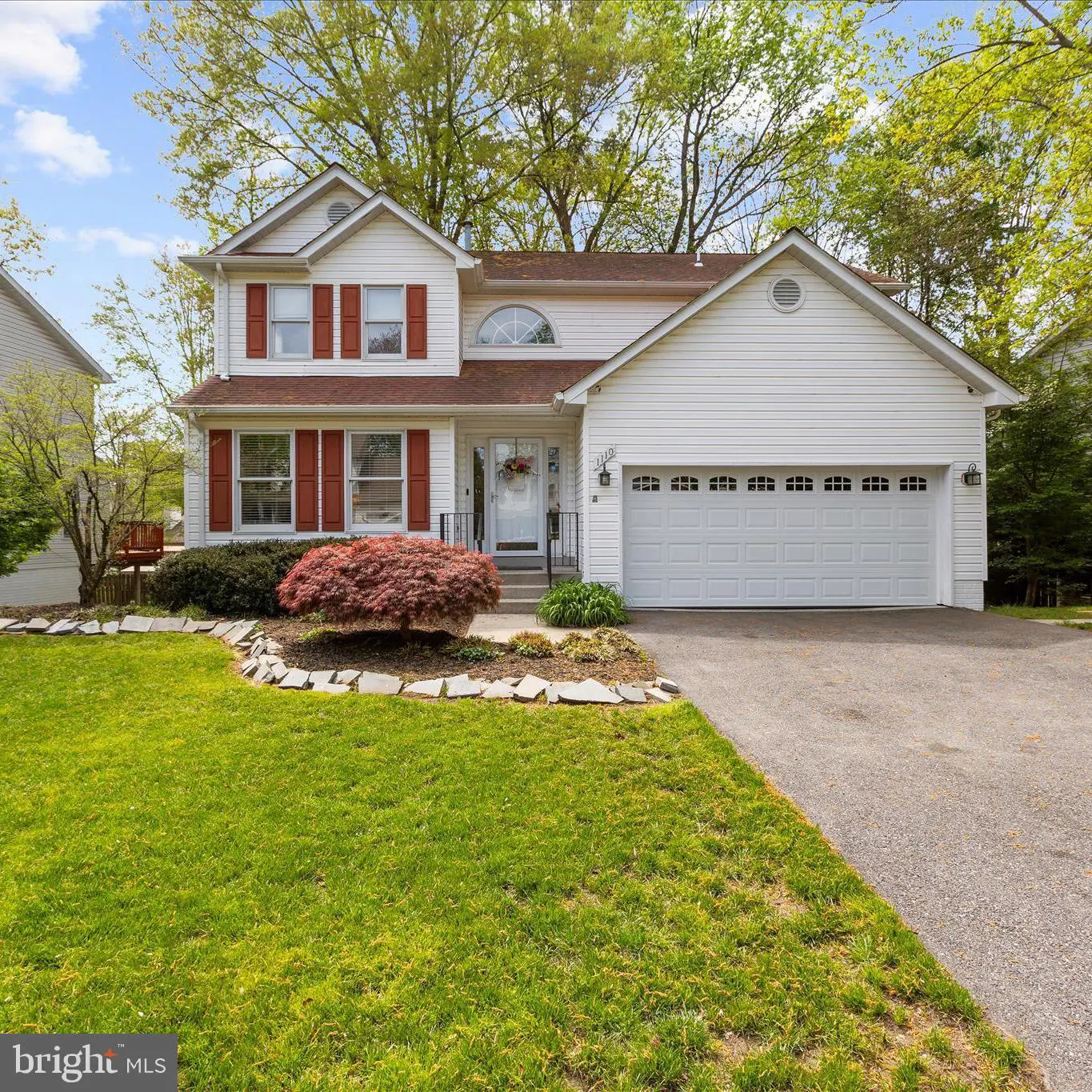 Two-story white house with red shutters, a green lawn, and a two-car garage on a sunny day.