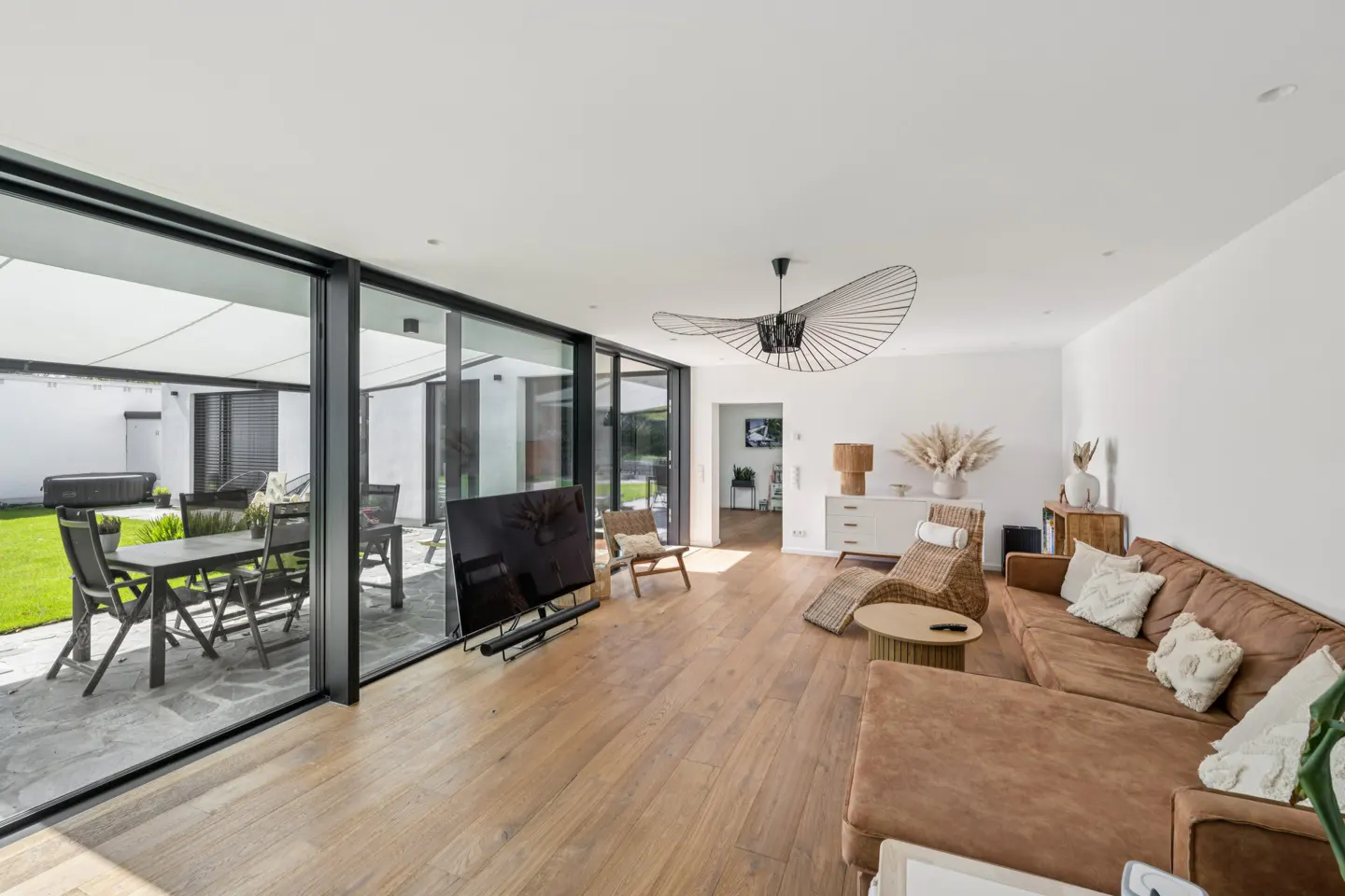 Bright living room with a brown sofa, wood floors, and large sliding glass doors to a patio with outdoor furniture.