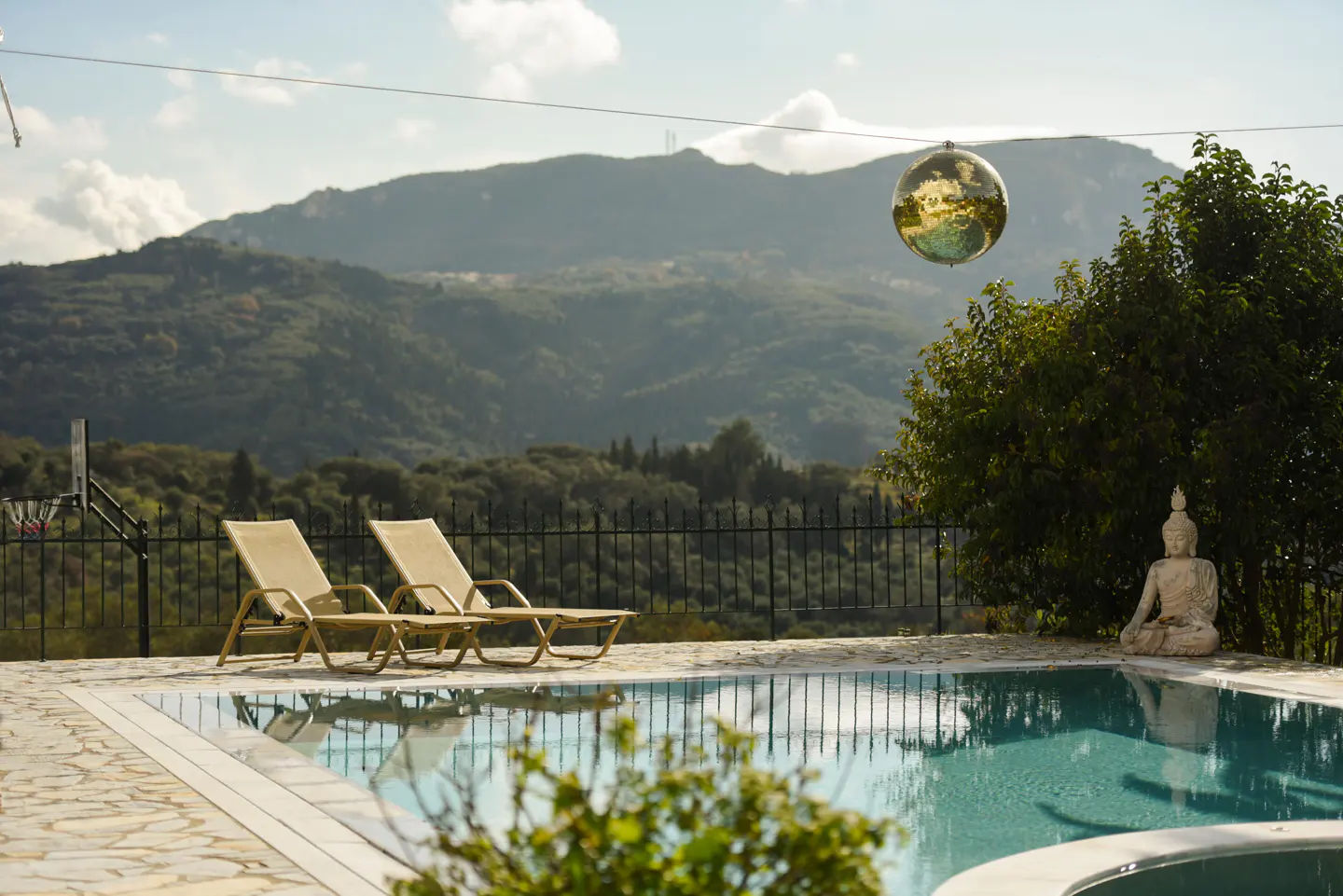 Outdoor pool with two lounge chairs, a Buddha statue, and a disco ball. Mountains are visible in the background.
