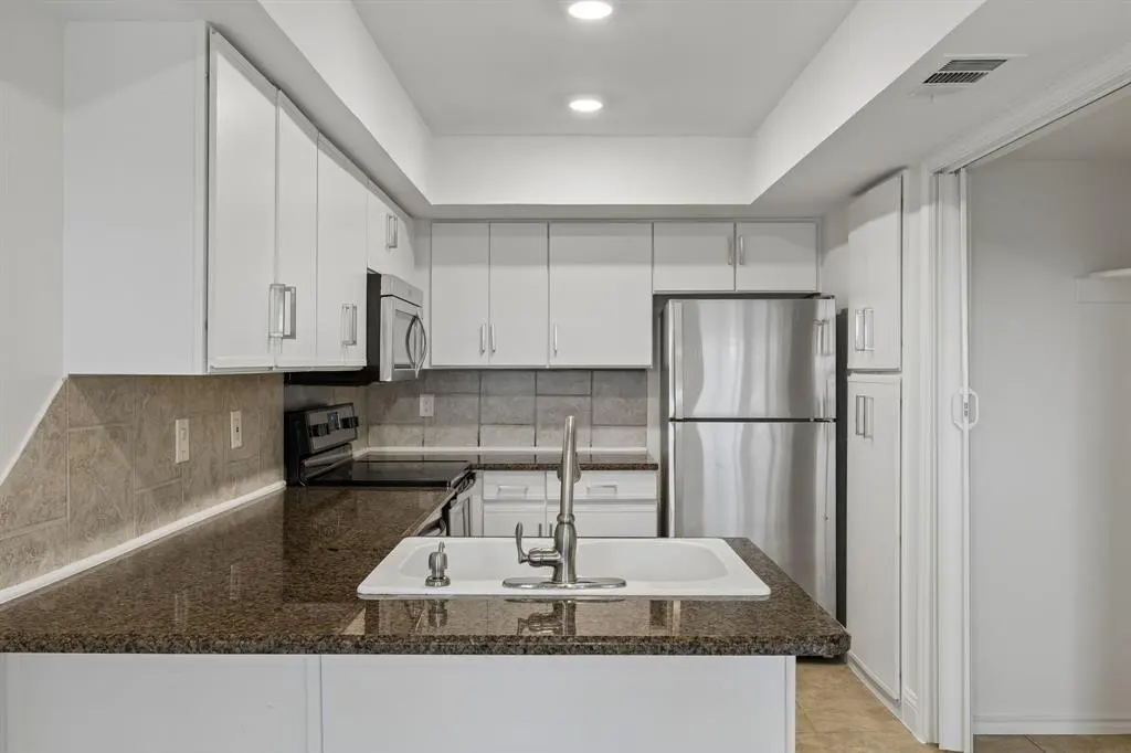 A kitchen with white cabinets, stainless steel appliances, and a dark granite countertop. A white sink is in the foreground.