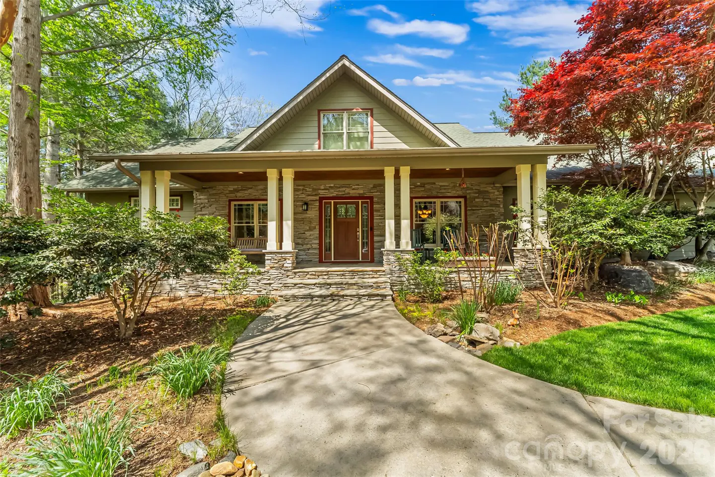 A single-story house with a stone facade, a covered porch with white columns, and a concrete walkway leading to the front door.