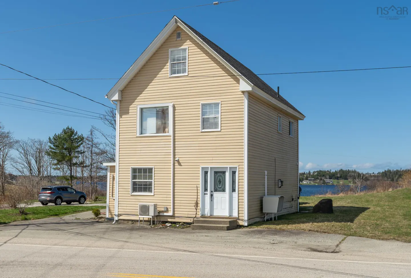 Two-story yellow house with white trim, a white front door, and a black roof under a clear blue sky. A car is parked nearby.