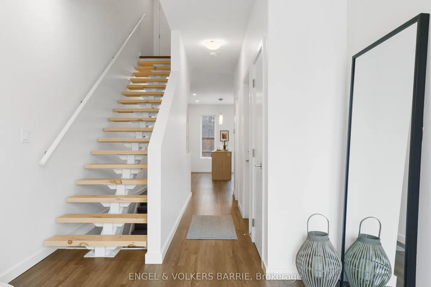 Bright foyer with wood floors, white walls, and open staircase. A full-length mirror and two gray lanterns are near the entrance.