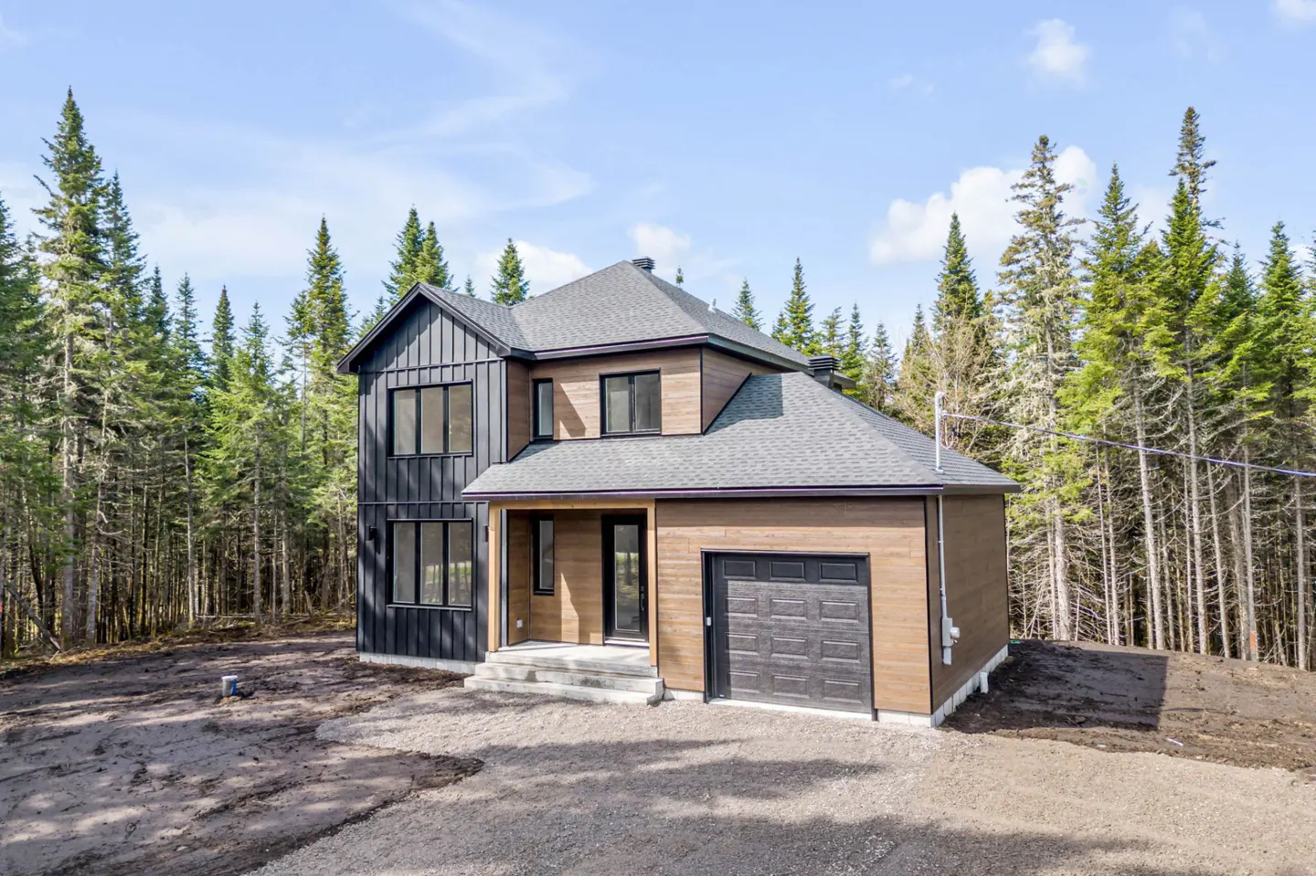 Two-story house with black and brown siding, gray roof, and a one-car garage, surrounded by tall green trees.