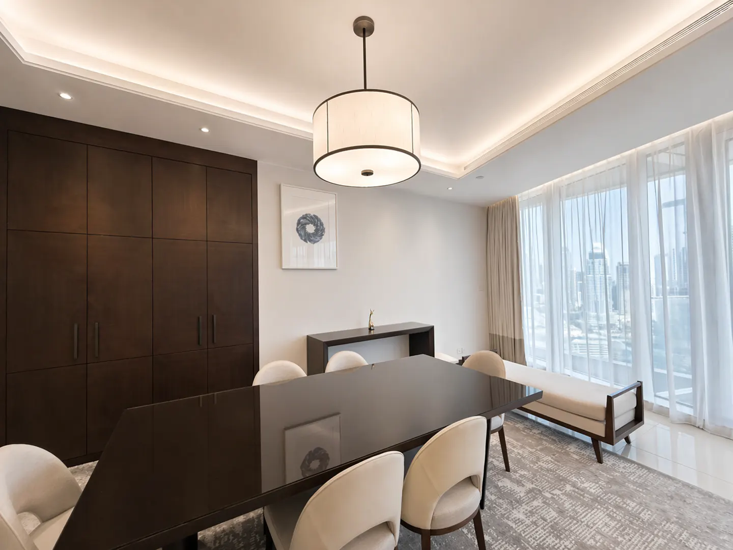 A modern dining room with a dark wood table, cream chairs, and a large window with city views.