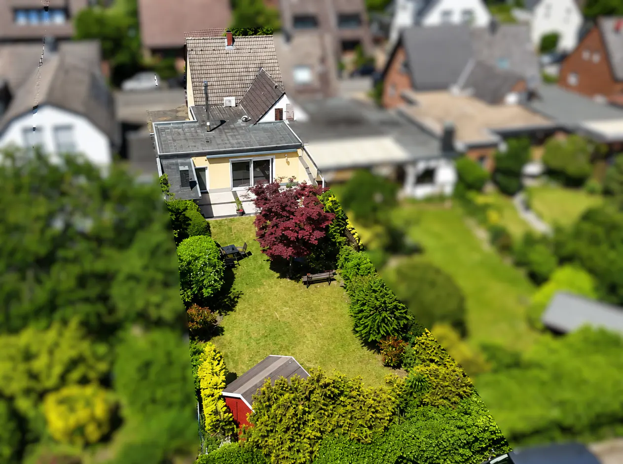 Aerial view of a house with a long, lush green backyard featuring a red Japanese maple, a small shed, and garden seating.