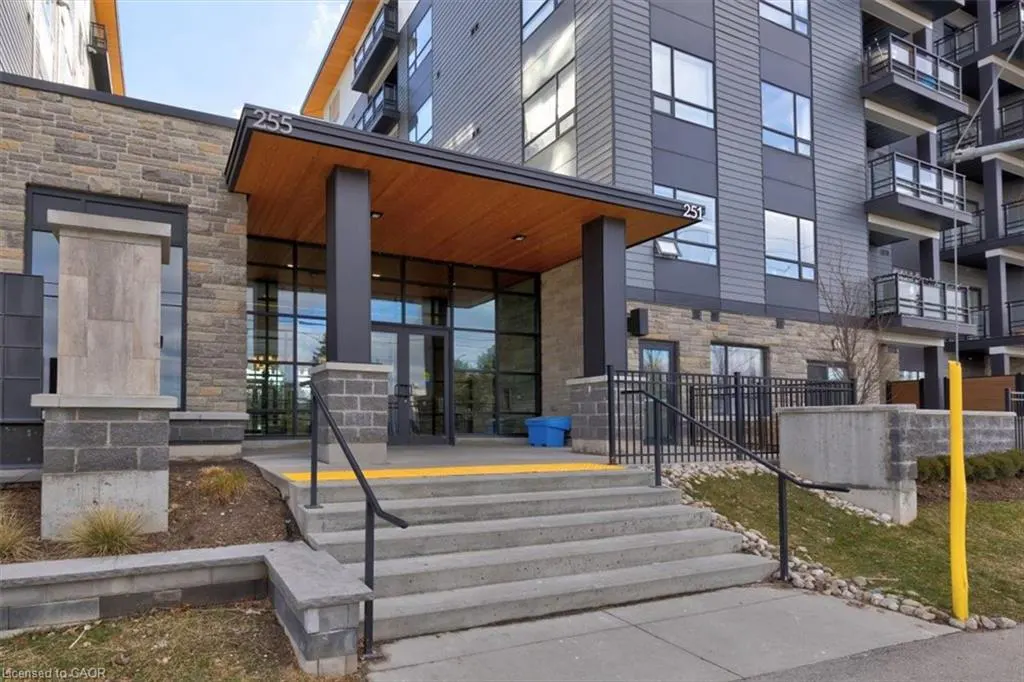 Exterior of a modern apartment building with stone and gray siding, featuring a covered entrance with glass doors and concrete steps.