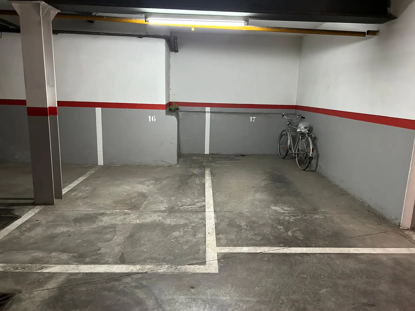 Indoor parking garage with numbered spaces, concrete floor, and a bicycle parked in space 17.