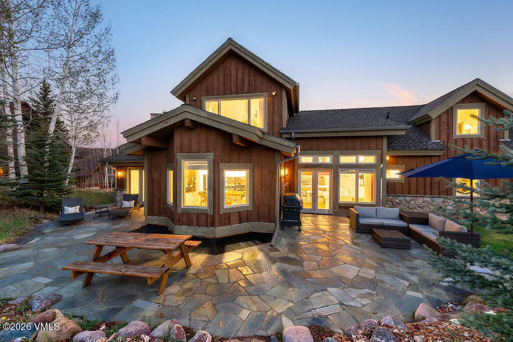 Exterior view of a brown wood house with a stone patio, picnic table, and outdoor seating at dusk.