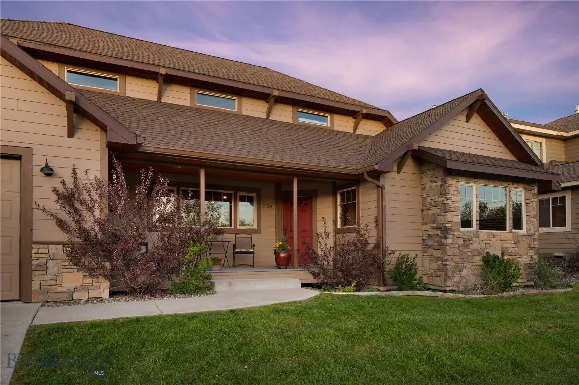 Tan two-story house with a brown roof, red front door, stone accents, and a green lawn.