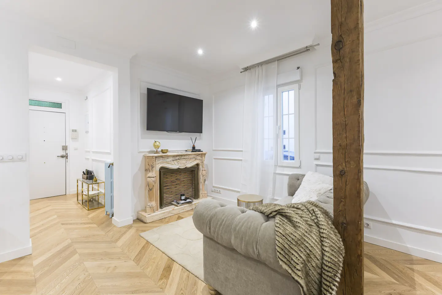 Bright living room with herringbone wood floors, a stone fireplace with TV above, and a gray sofa with a throw blanket.