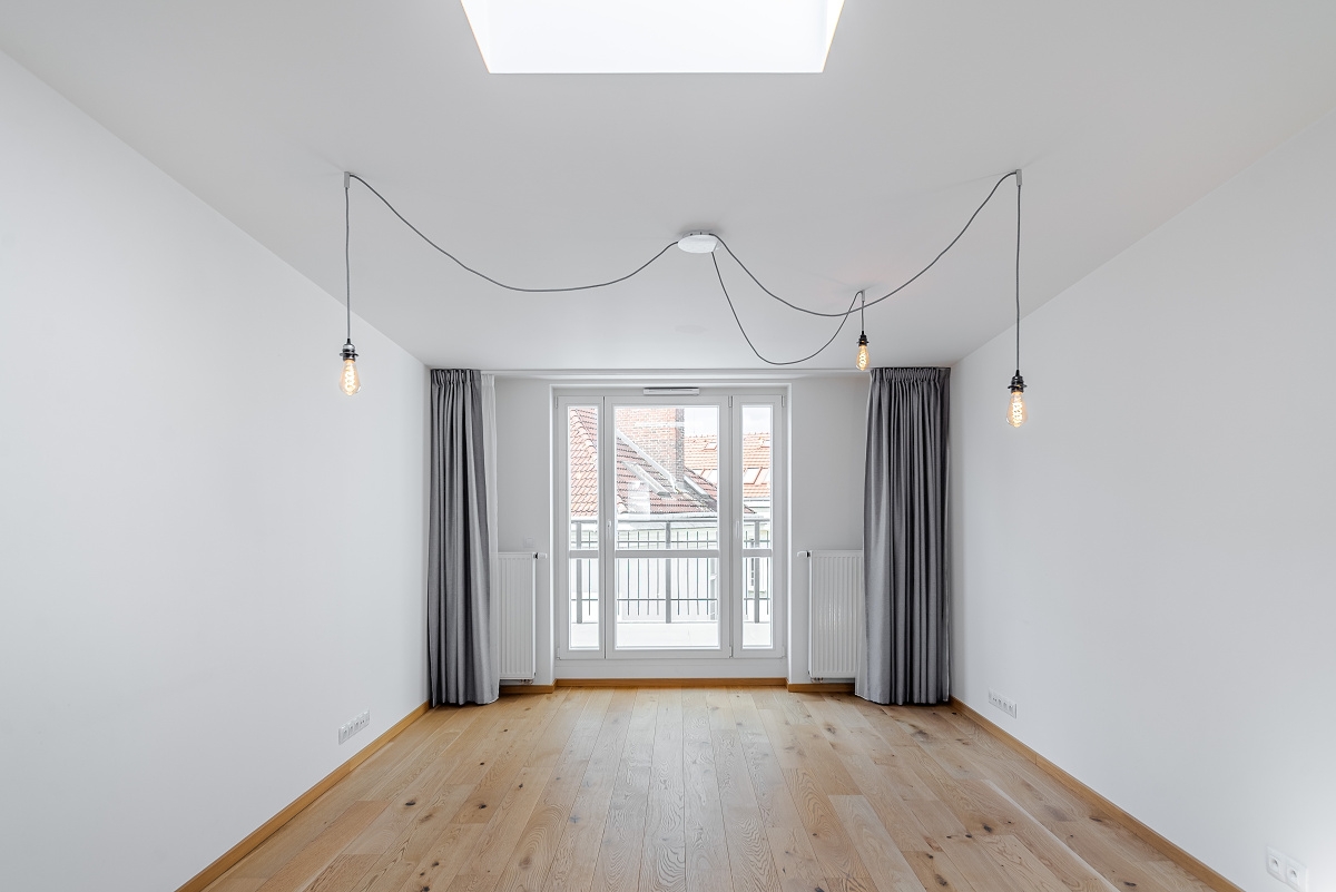 Minimalist room with white walls, light wood floors, grey curtains, and three hanging Edison bulbs over a balcony door. [AI-generated text]
