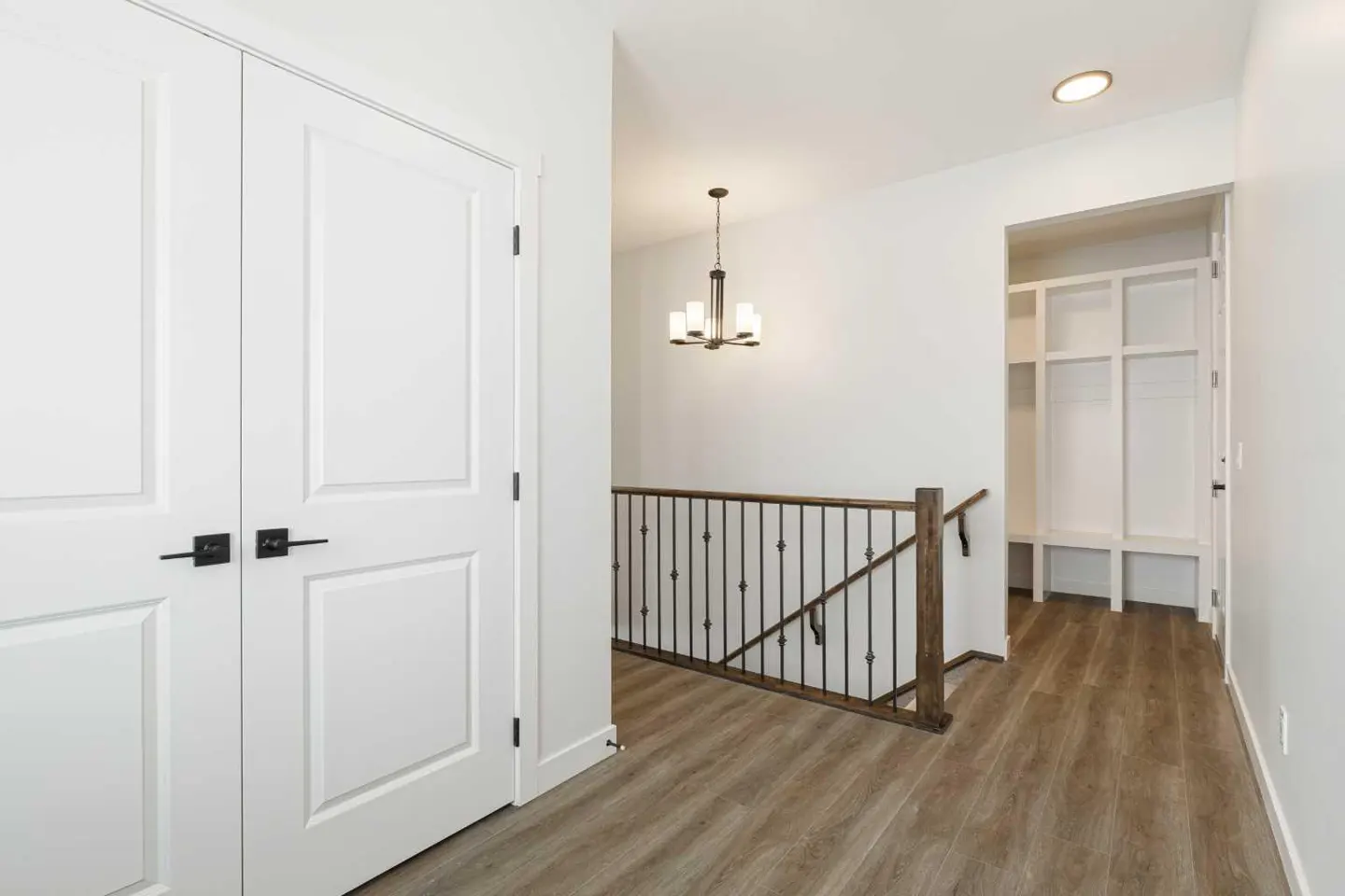 Hallway with wood-look floors, white walls, and a staircase with a dark metal railing. White closet doors are on the left.