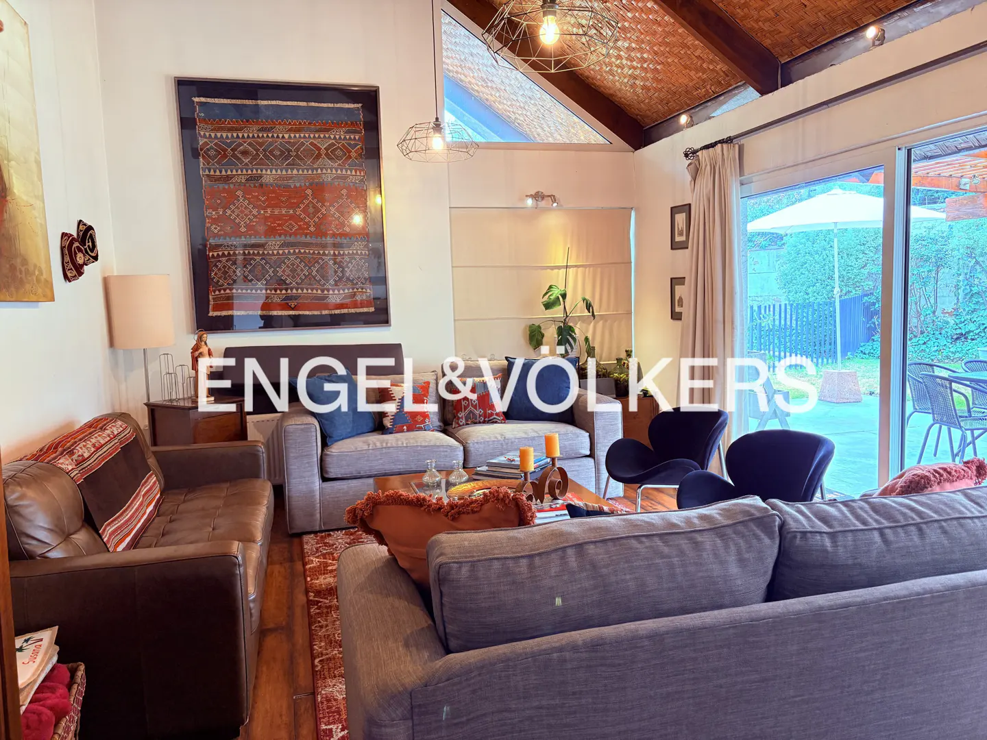 Living room with gray sofas, brown leather couch, and black chairs. A large rug and art adorn the space, with a view to the backyard.