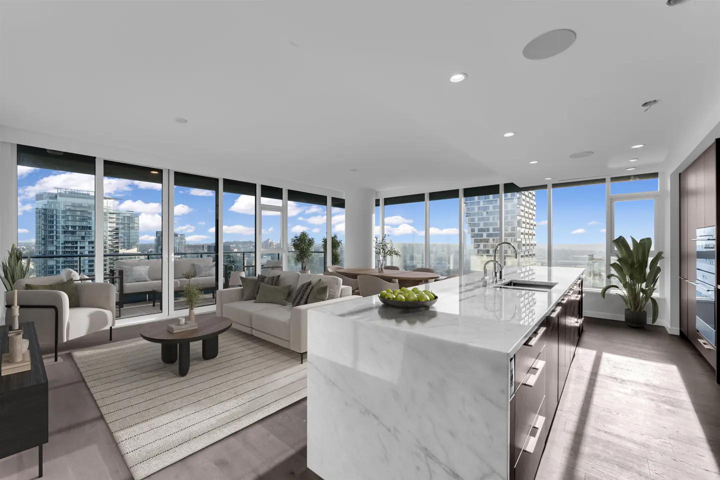Bright, open condo with floor-to-ceiling windows. Living area with sofa, chairs, and rug. Kitchen island with marble countertop and city view.