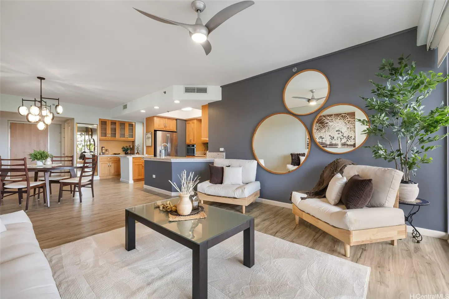 Open-concept living space with wood floors, a gray accent wall with round mirrors, and a modern kitchen.