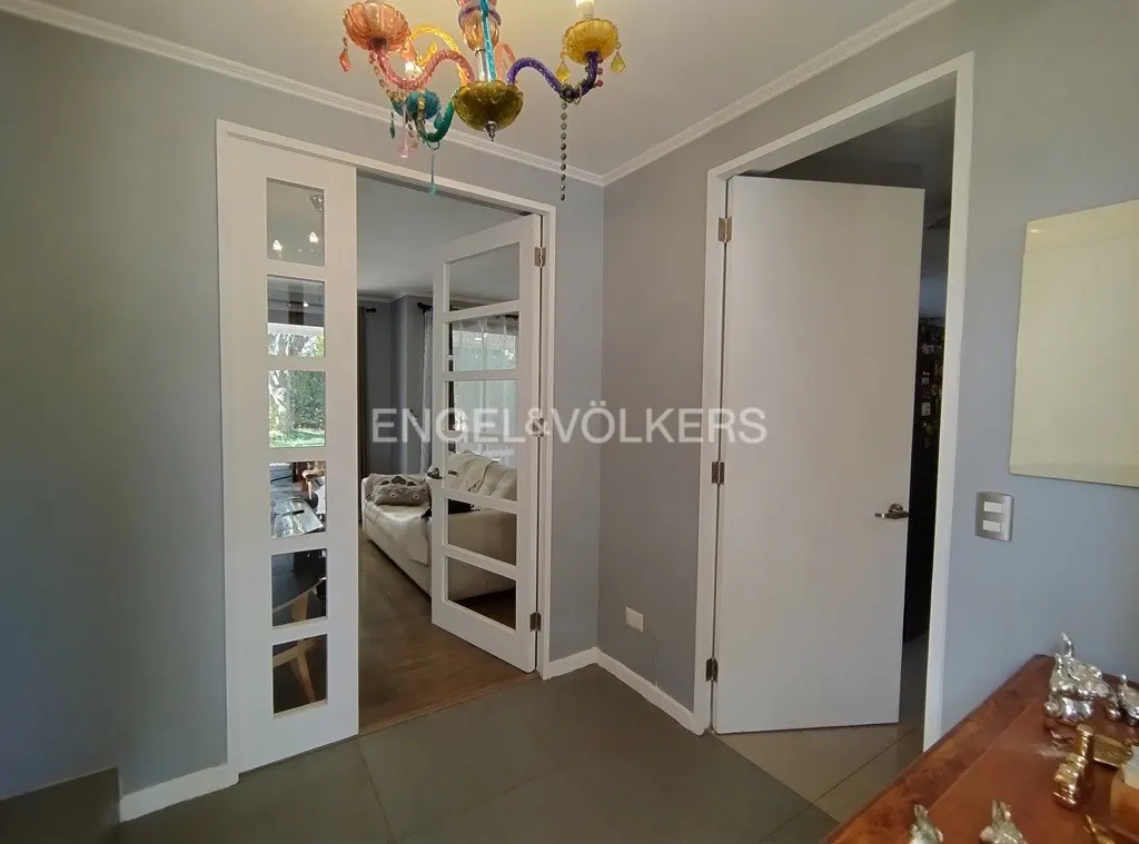 Hallway with gray walls, white trim, and a colorful chandelier. Glass paneled doors lead to a living room with a white sofa.