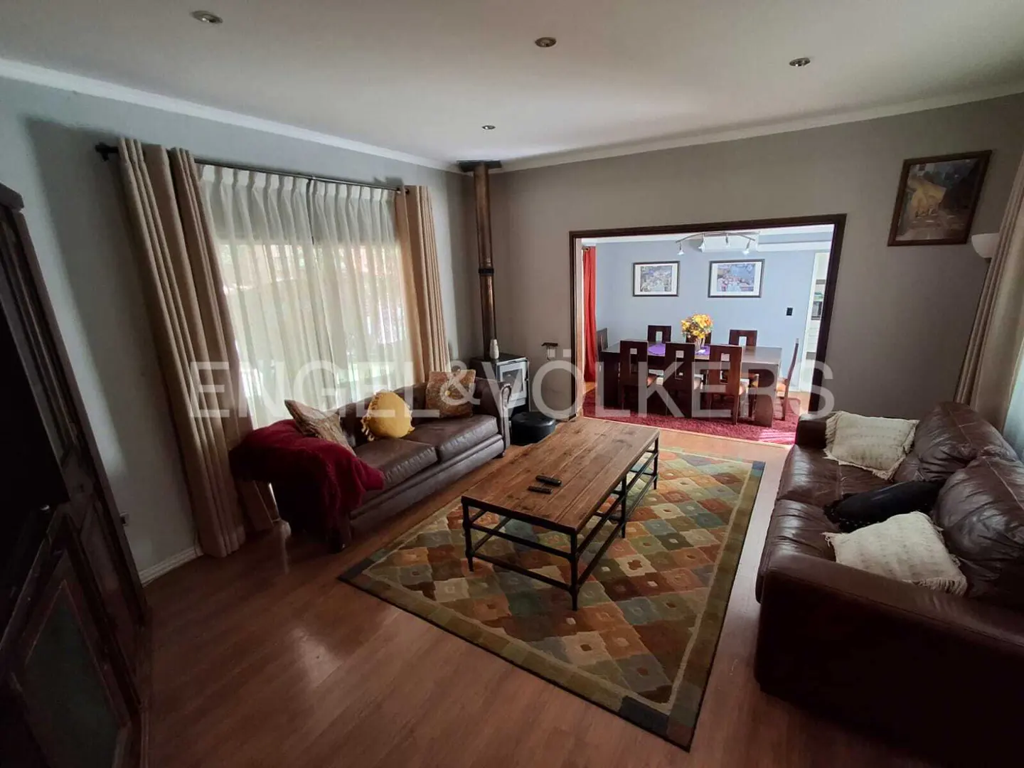 Living room with hardwood floors, two brown leather sofas, a wood coffee table, and a colorful patterned rug. A dining room is visible through an archway.