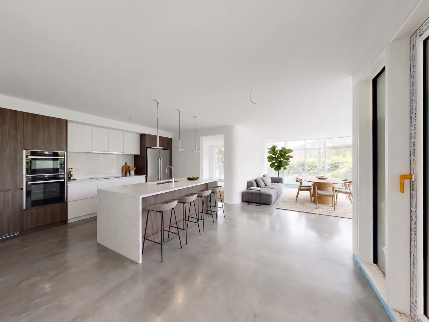 Open-concept kitchen and living area with a large island, modern cabinets, and gray seating. A dining table and sofa are in the background.