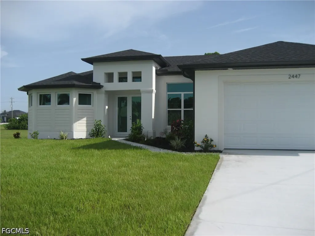 Modern white single-story home with a dark roof, two-car garage, and green lawn under a clear blue sky.