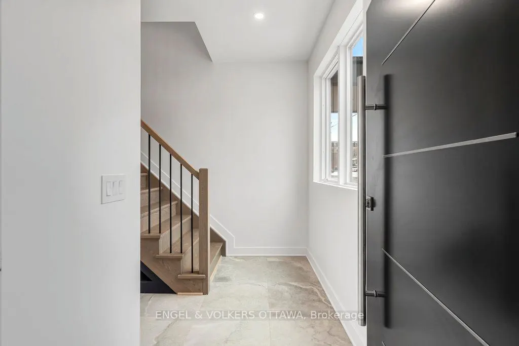 Open black front door reveals a modern foyer with a staircase, window, and light gray tile floor.