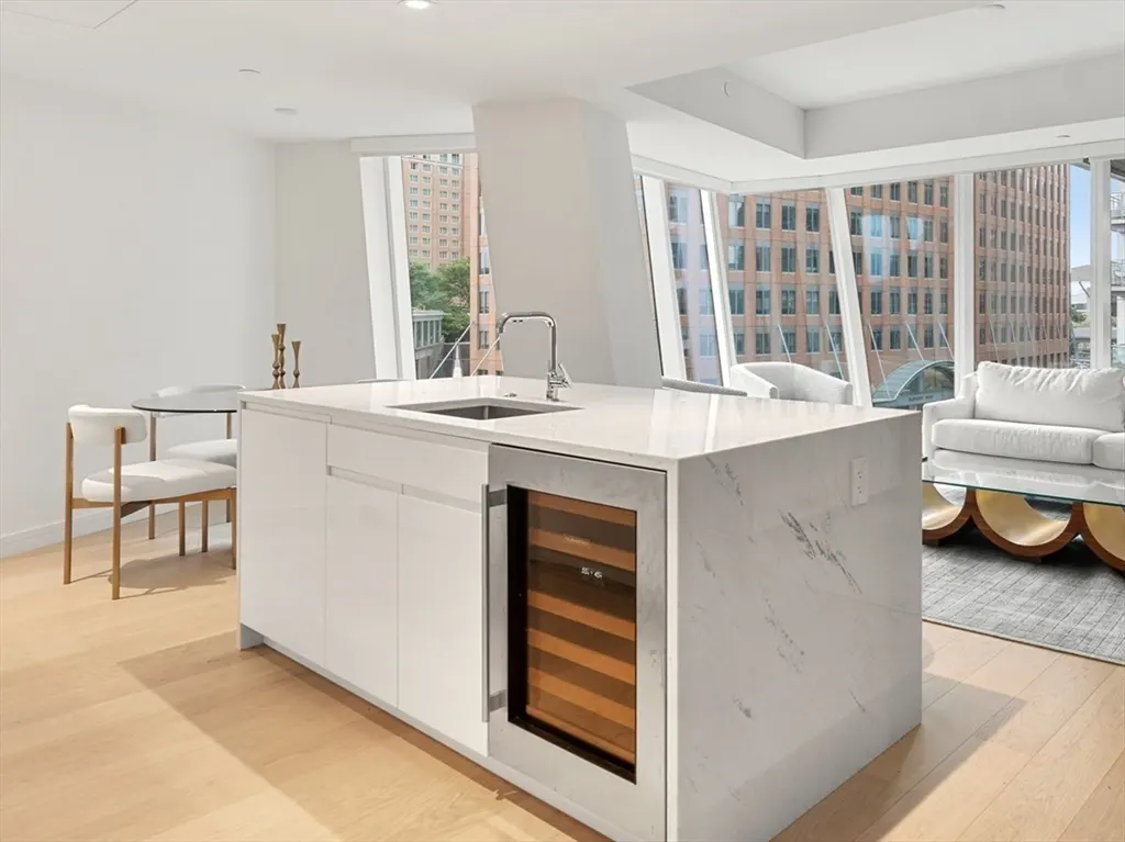Bright, modern kitchen with a marble island, stainless steel sink, and wine cooler. Large windows offer city views.