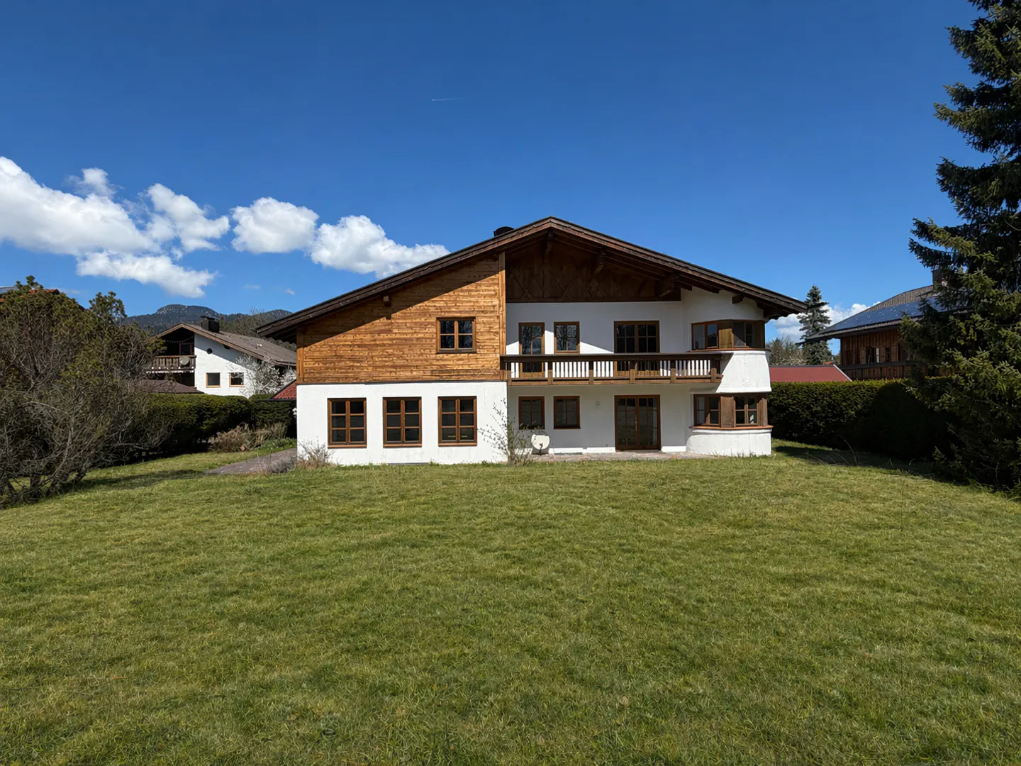 Two-story house with white walls and wood paneling under a blue sky. A green lawn stretches in front of the house.