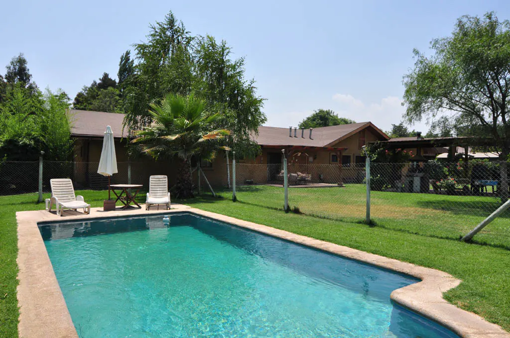 A backyard with a turquoise pool, two white lounge chairs, a small table, and a house in the background.