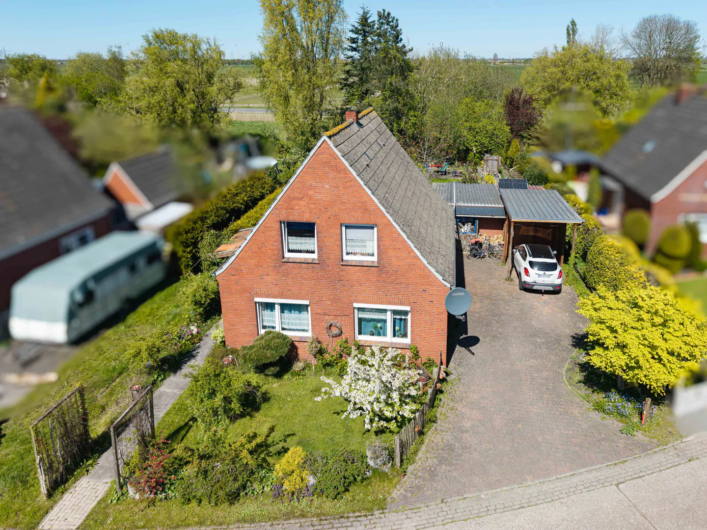 Aerial view of a red brick house with a gray roof, green lawn, and a white car parked in the driveway.