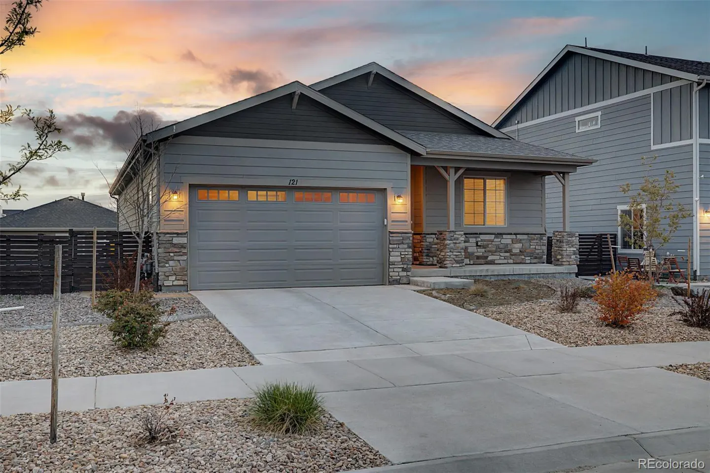 Gray single-family home with a two-car garage, stone accents, and a concrete driveway at dusk.