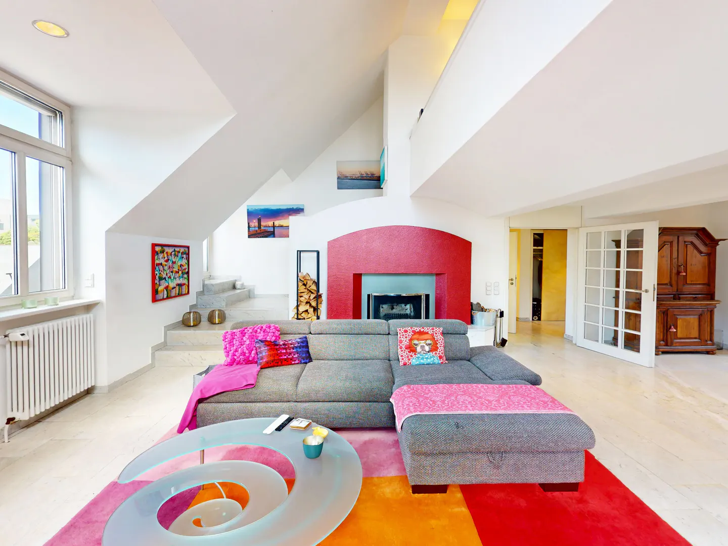 Bright living room with a gray sectional sofa, a red fireplace, and a spiral glass table on a colorful rug.