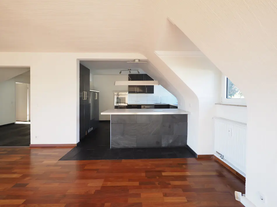 Bright, open apartment with hardwood floors and a modern kitchen. White walls and an angled ceiling add character.