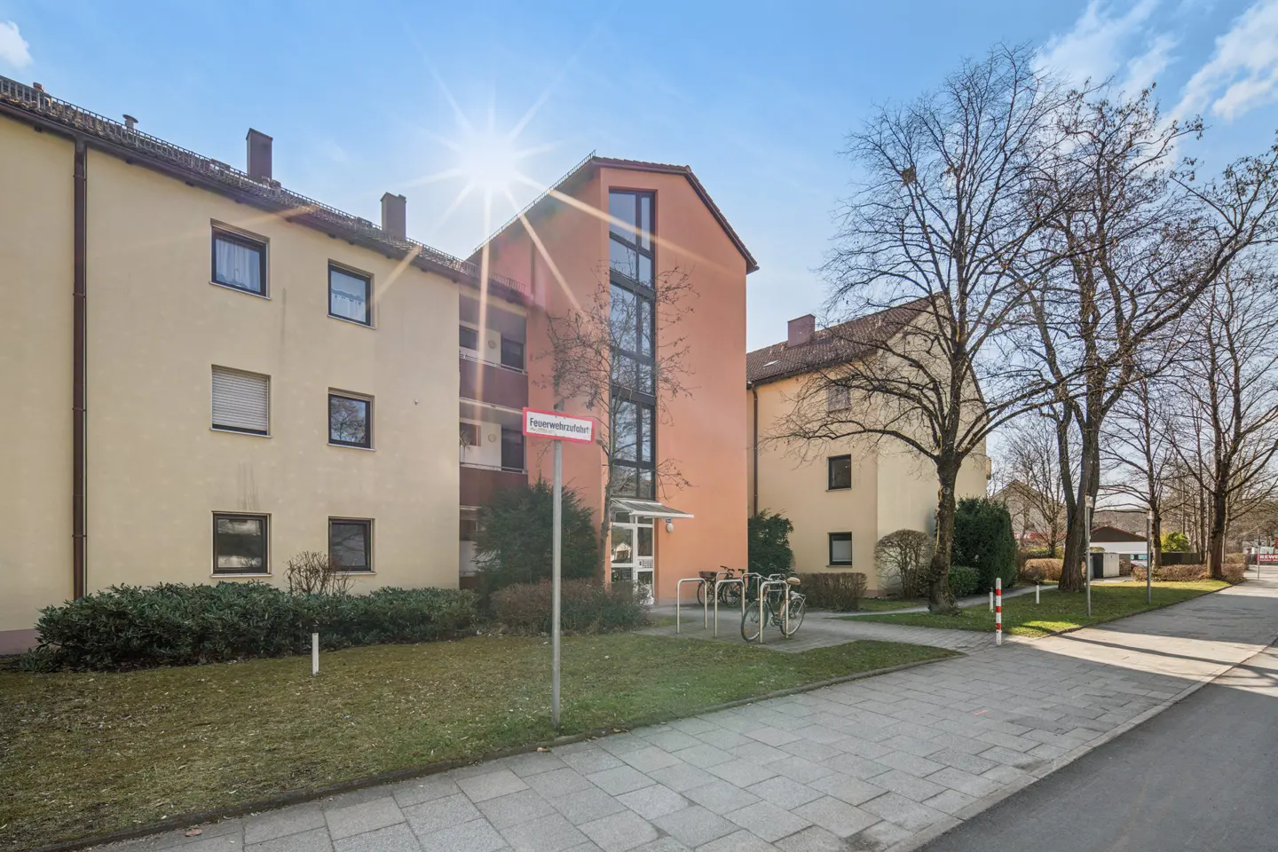Exterior view of a multi-story apartment building with a peach-colored facade and a bike rack near the entrance.
