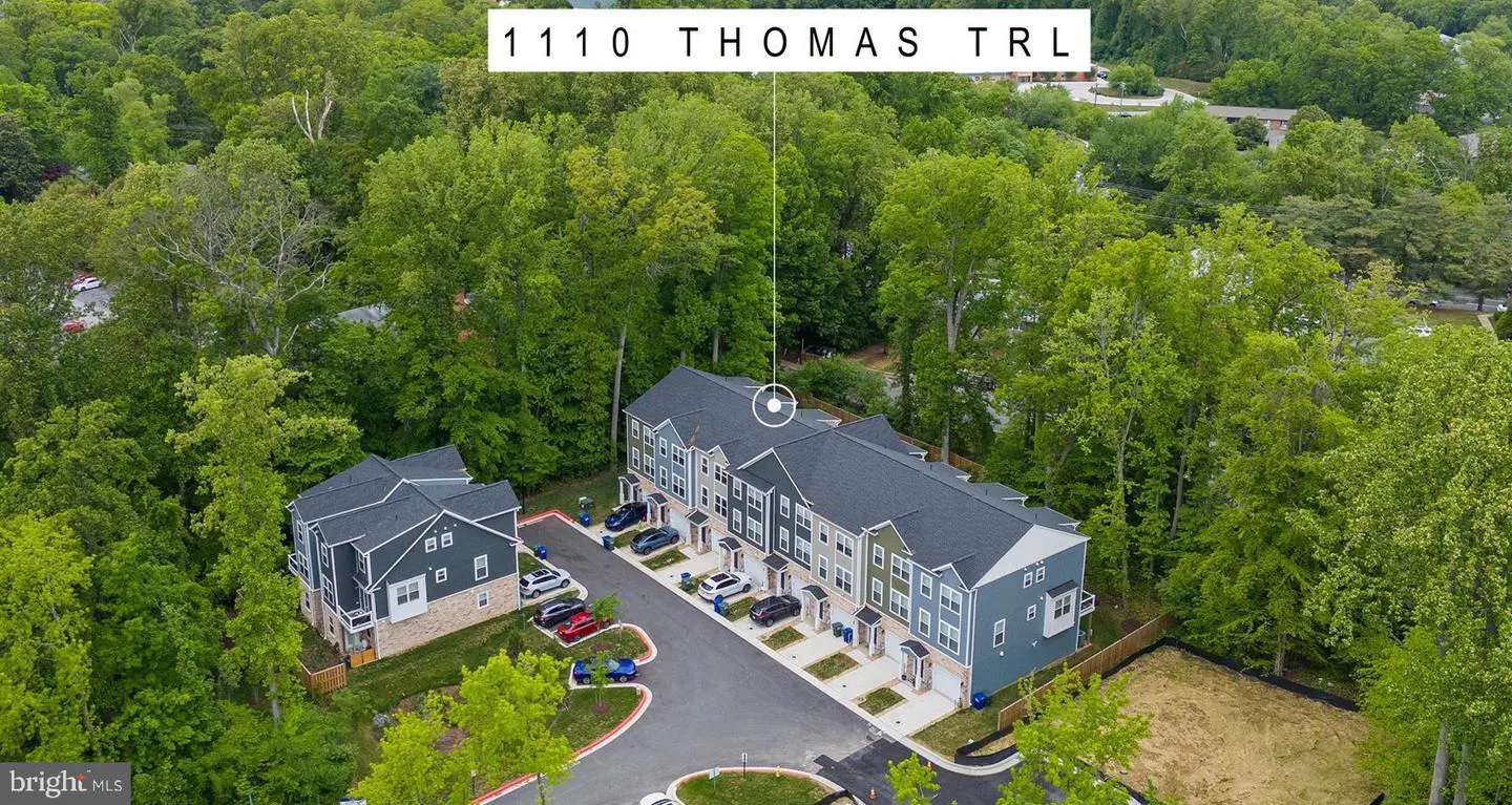 Aerial view of 1110 Thomas Trl, showing modern townhouses with gray roofs, surrounded by lush green trees and parked cars.