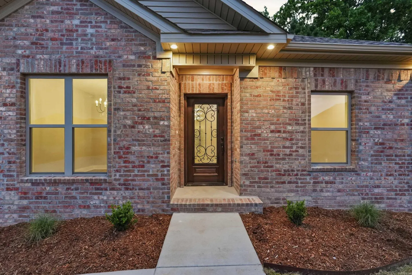 Brick house exterior with a decorative glass front door, two windows, and a concrete walkway.