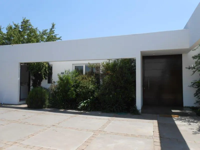 Modern white house exterior with a dark brown door, green bushes, and a concrete tile driveway under a clear blue sky.