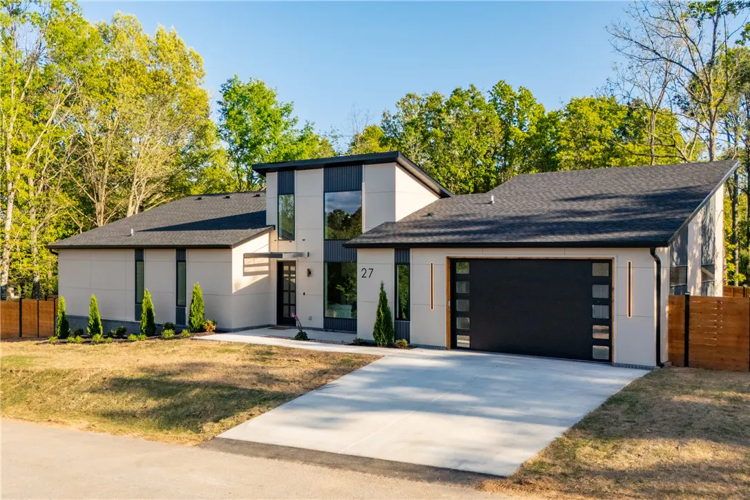 Modern beige house with black trim, dark roof, and a black garage door with square windows. The house number "27" is visible.