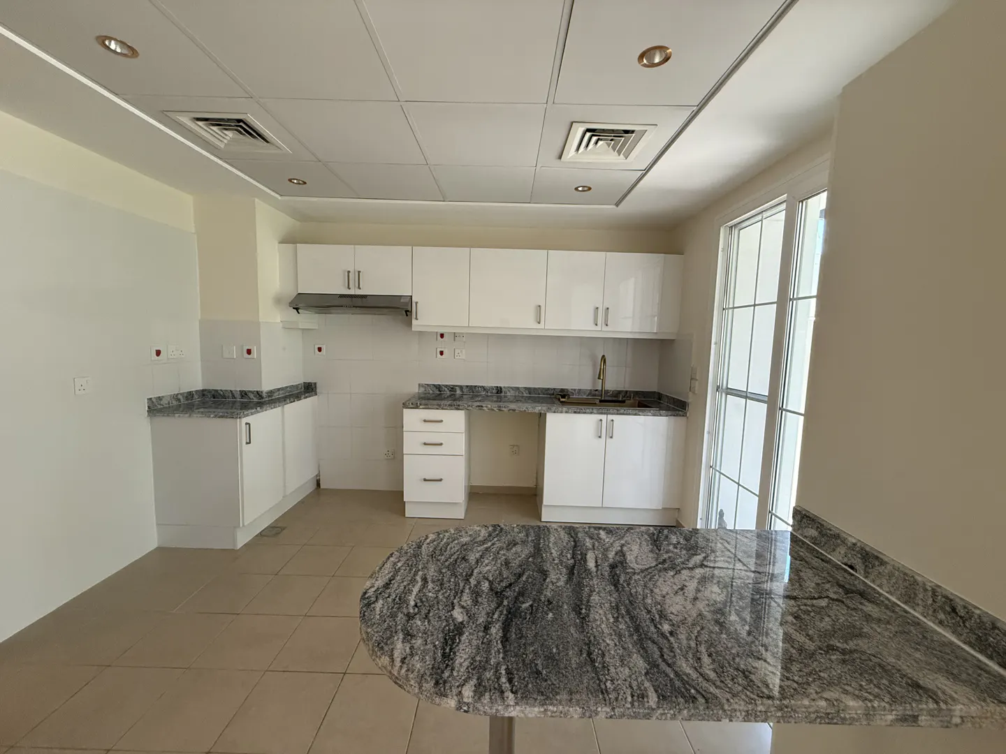 A bright kitchen with white cabinets, gray granite countertops, and a breakfast bar. A window lets in natural light.
