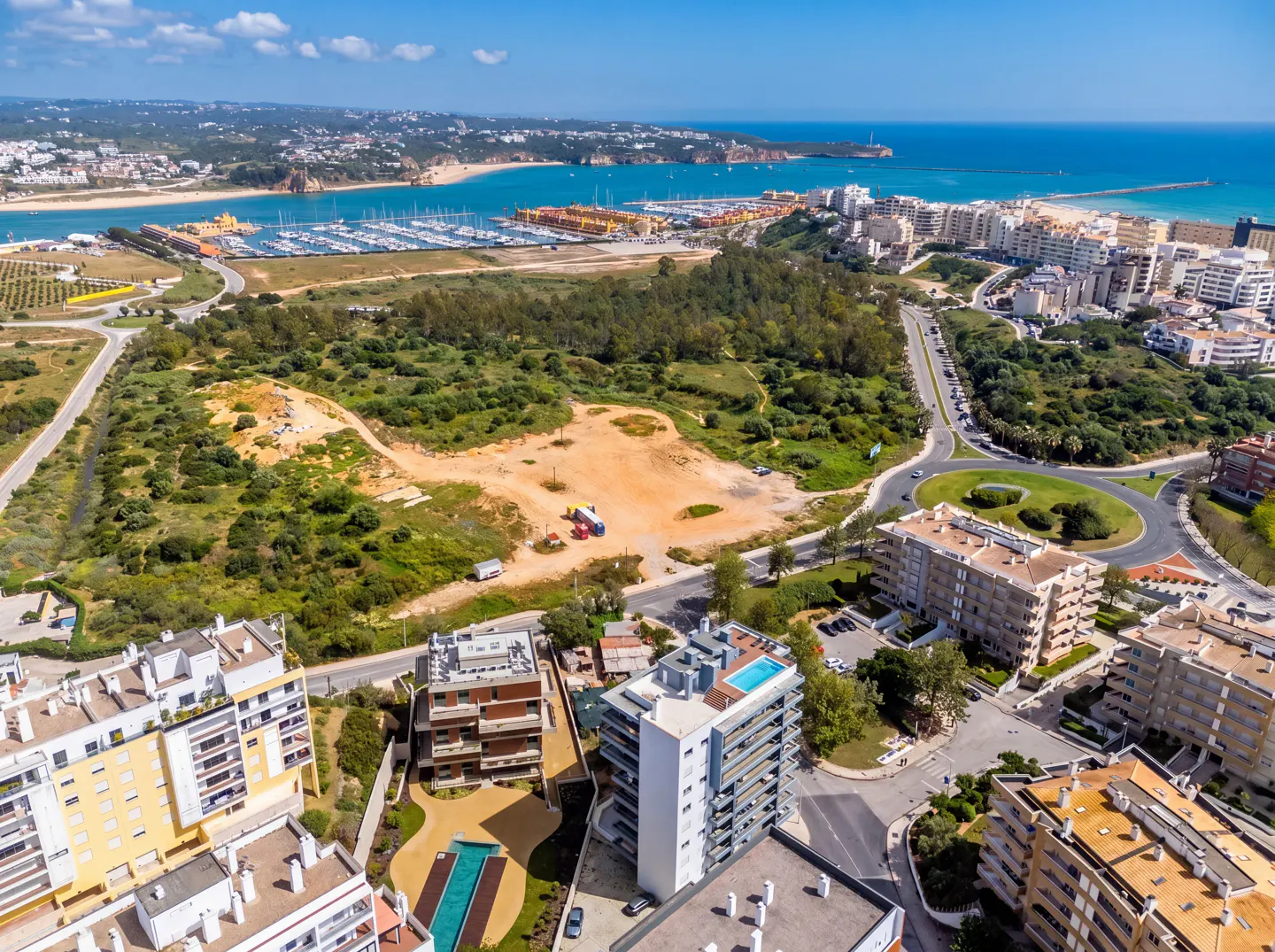 Aerial view of coastal real estate with apartments, a marina filled with boats, and a sandy beach under a clear blue sky.