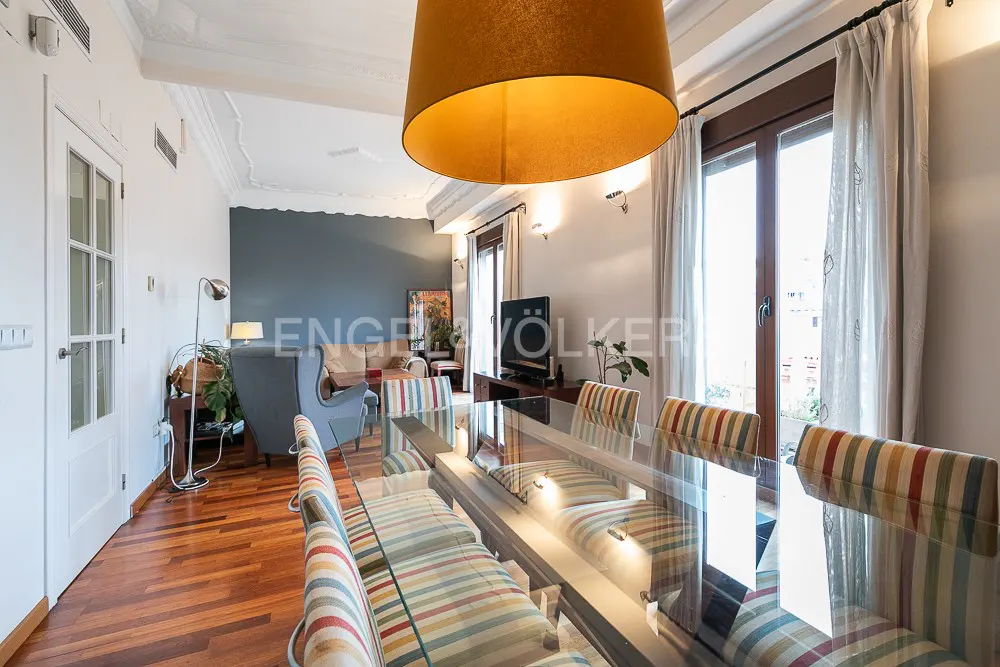 Bright dining room with a glass table, striped chairs, and a large yellow pendant light. Living room visible in the background.