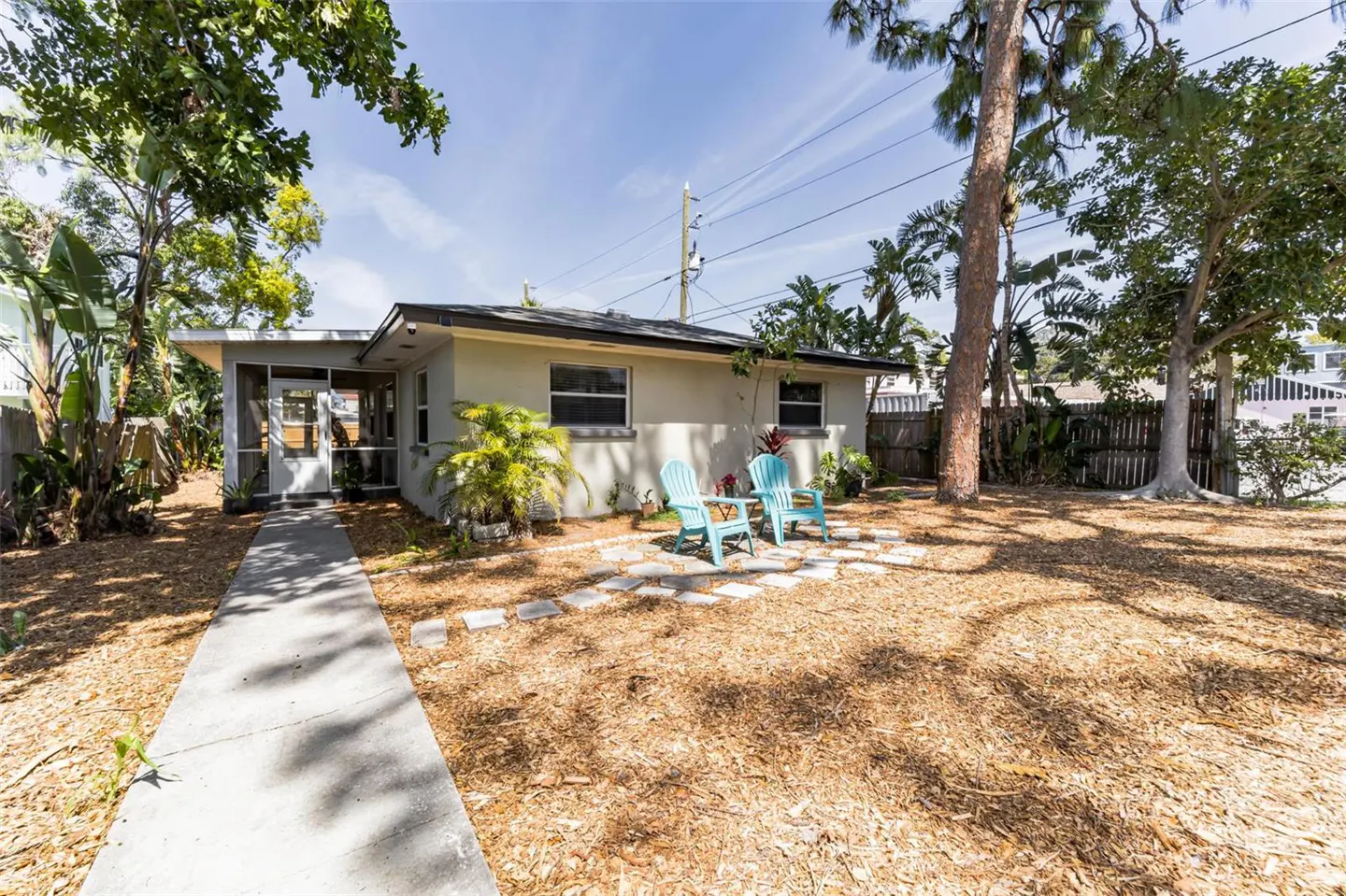Exterior of a one-story beige house with a screened-in porch, a concrete walkway, and two blue Adirondack chairs.