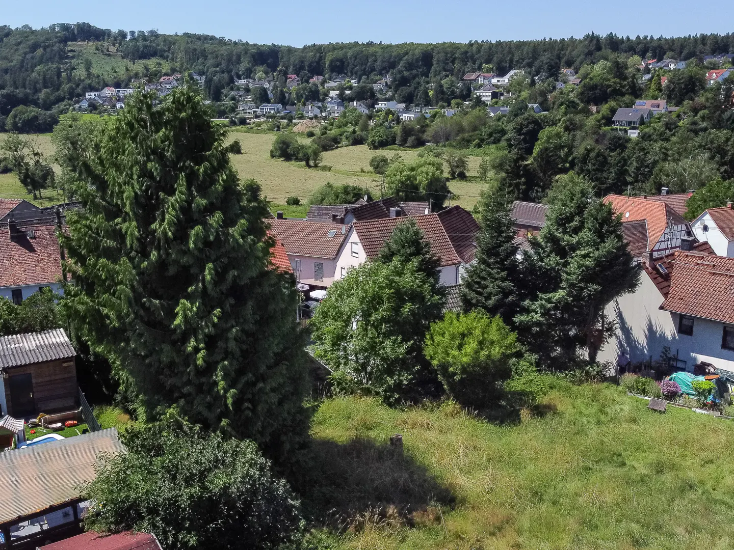 View of a village with houses, trees, and a green field under a blue sky.