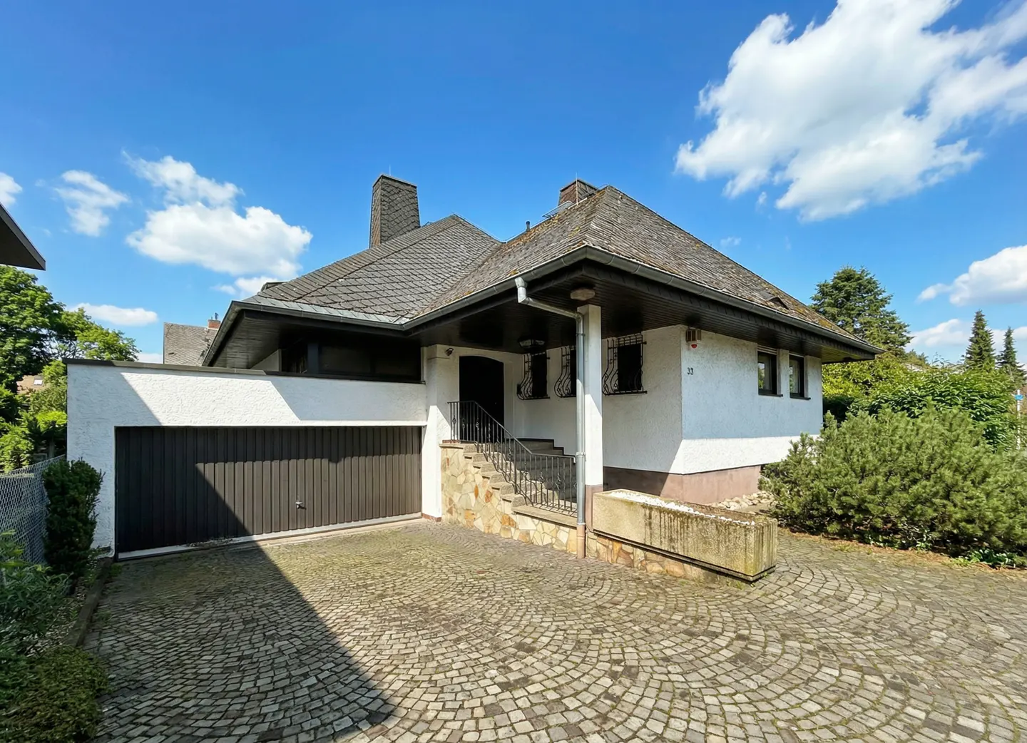 Exterior of a white, one-story house with a brown garage door and stone driveway under a blue sky.